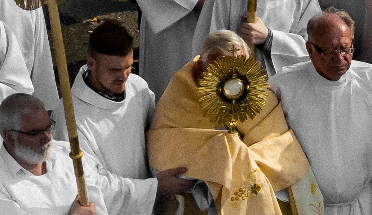 Priests in white robes carrying a gold monstrance during a religious procession